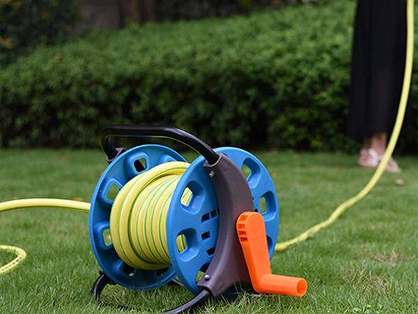 A woman is holding the hose of garden hose reel watering the grass.