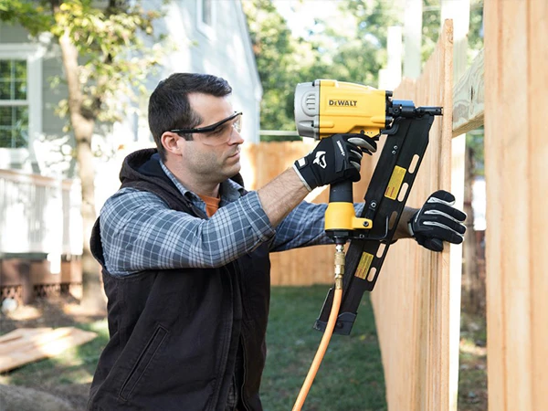 A person is using a brad nailer with a yellow PU air hose to secure wooden boards