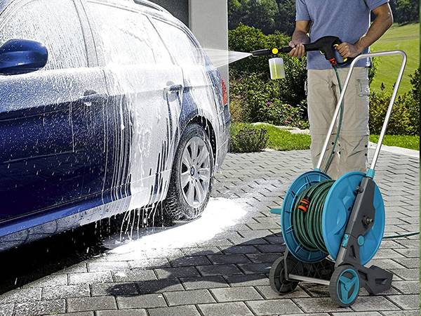 A man is holding retractable garden hose reel to wash the car.