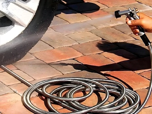 A person is holding the nozzle of a stainless steel garden metal hose washing a car tire.