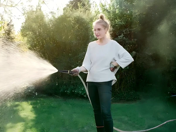 A girl is holding the nozzle of a stainless steel garden metal hose watering flowers in the garden.